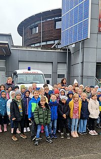 Eine Gruppe von Kindern und Erwachsenen posiert vor einem Krankenwagen 