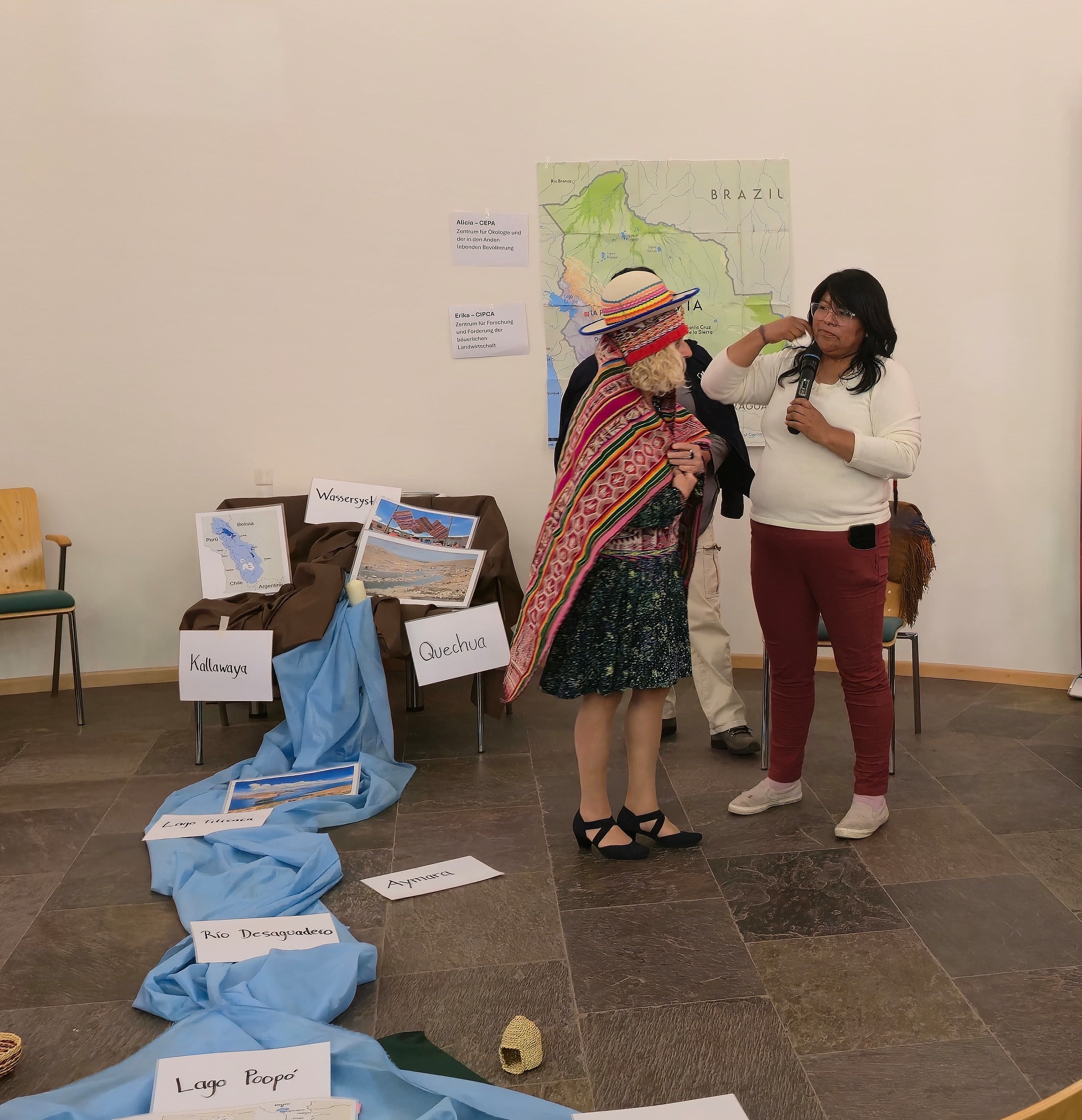 Eine Referentin aus Bolivien kleidet eine Teilnehmerin mit traditioneller Kleidung aus dem Altiplano ein und erklärt deren Bedeutung.