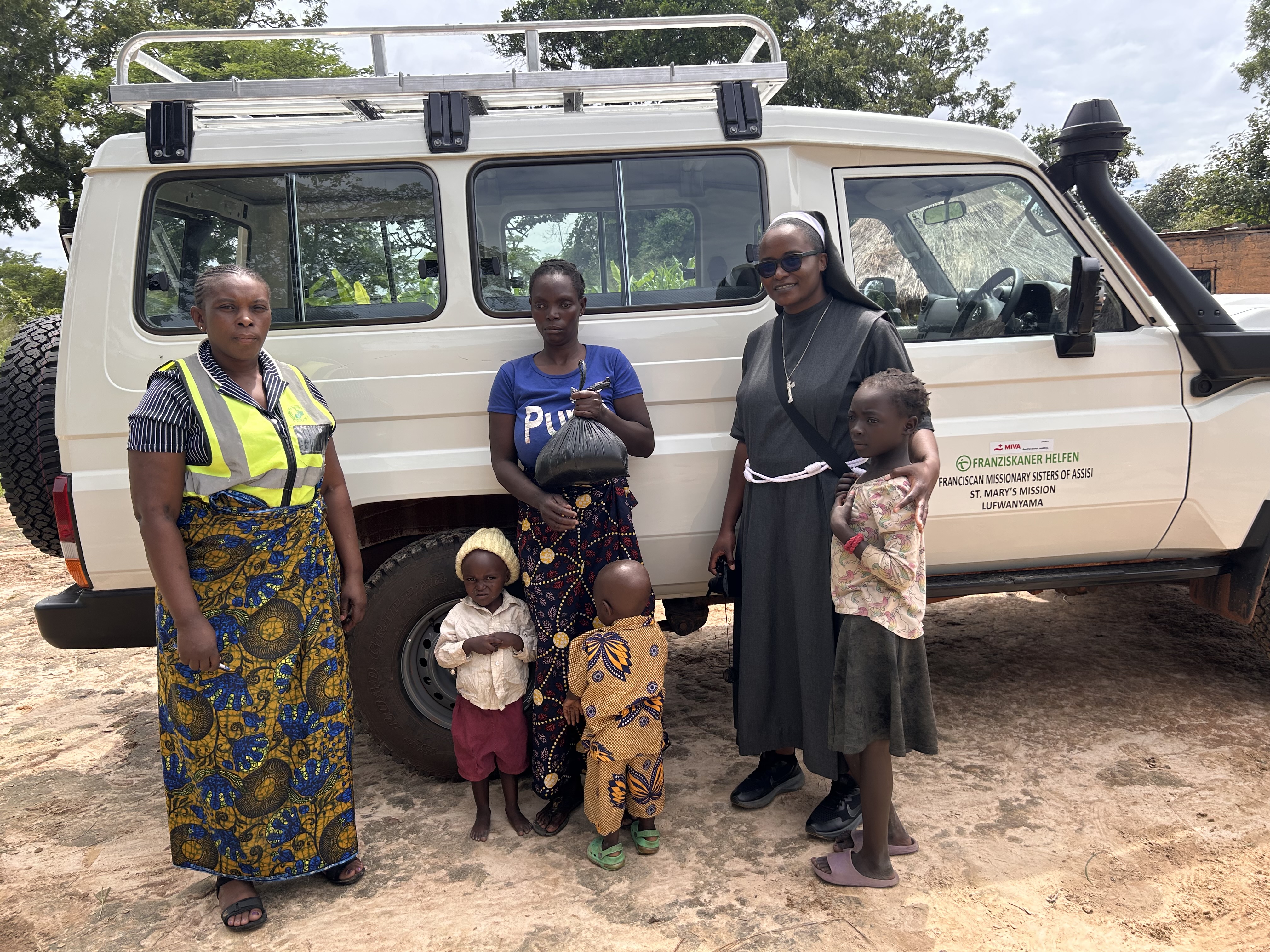 Franciscan Missionary Sisters of Assisi mit Familien vor einem MIVA-Fahrzeug in Lufwanyama, Sambia, das für Outreach-Programme zur Versorgung von HIV-betroffenen Kindern und Familien eingesetzt wird.